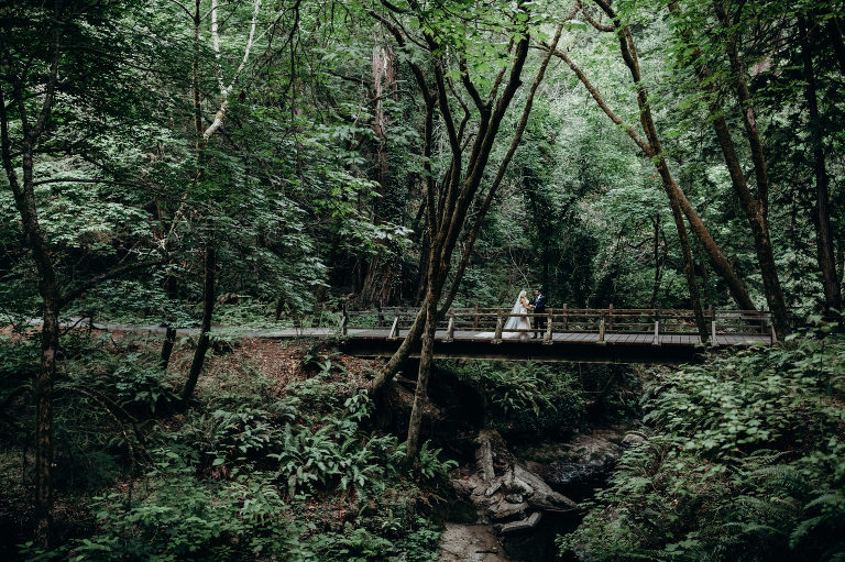 A Newlywed couple stands on a bridge at Island Farm, one of the best redwood forest venues in California